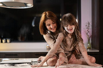 Daughter and mother cook in the kitchen using flour