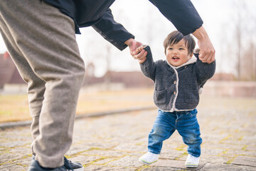 外でパパと一緒にあんよ（歩く）練習をして楽しそうな笑顔を見せる1歳の赤ちゃん