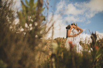 mujeres jovenes al aire libre usando su vestido de bodas mientras se besan en medio de la...