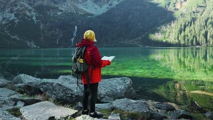 Woman traveler explorer with backpack hiking to the top of the mountain. Tourist hiker senior woman backpacker in mountain read the map. 