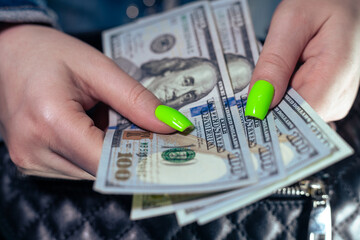 A woman with green manicure counts money. One hundred dollar bills in female hands