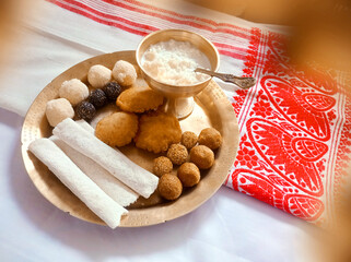 Assamese traditional food items like pitha, laddu, doi sira with assamese gamosa background with...