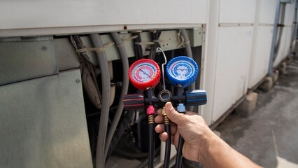 Air conditioning, HVAC service technician using gauges to check refrigerant and add refrigerant.	