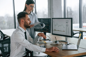 Fototapeta premium Woman is standing and holding documents. Two employees are working in the office together