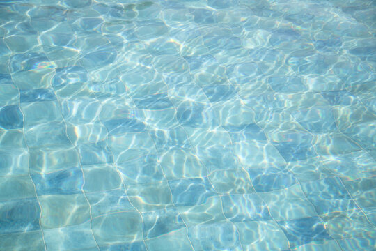 blue water surface background of swimming pool with tiles in sun light