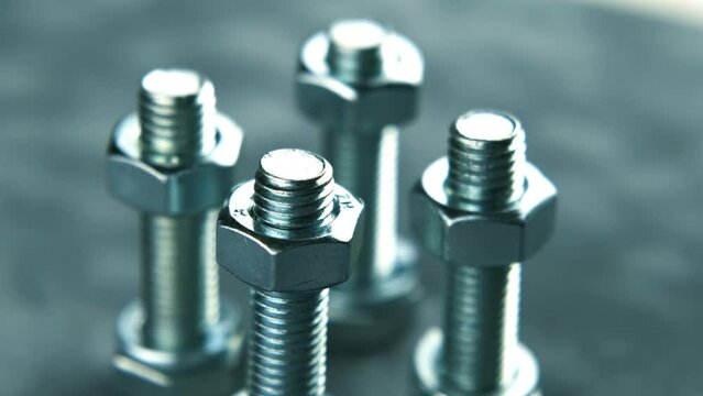 A group of bolts with washers and nuts for fastening, on a gray background, are slowly spinning.