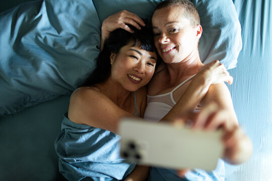Young lesbian couple taking selfie in bed