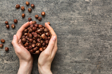 Woman hands holding a wooden bowl with hazelnut nuts. Healthy food and snack. Vegetarian snacks of...