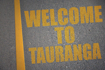 asphalt road with text welcome to Tauranga near yellow line.