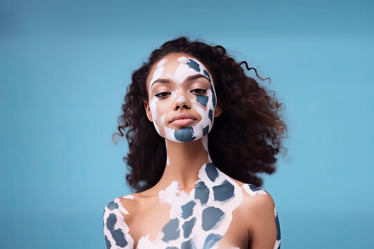 Sensual woman with painted spots on her face and body, standing against a blue background.