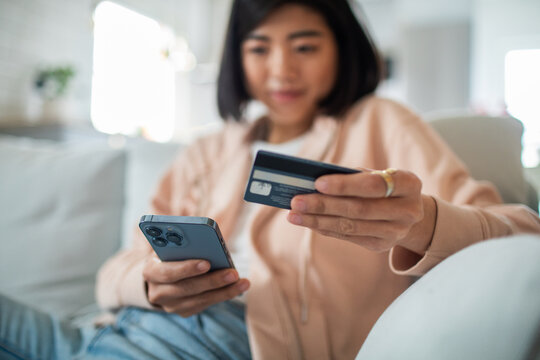 Smiling young adult woman using credit card on smartphone at home