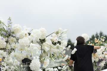 Professional wedding decorator arranging fresh flowers on an outdoor arch