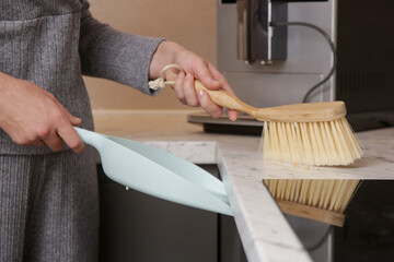 Close up image of woman's hands cleaning apartment with small broom and dustpan	