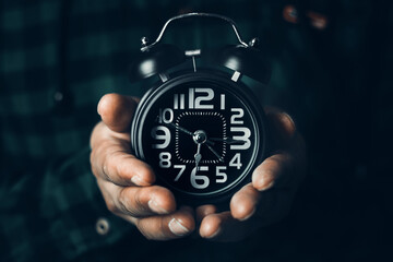 Time management concept. Man hands holding Black retro alarm clock. Time to wake up for the morning routine