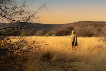A woman stands in grassland that glows golden in the early morning sun near Mount Etjo in central...