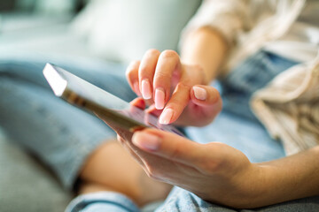 Close up woman sitting on couch using smartphone at home