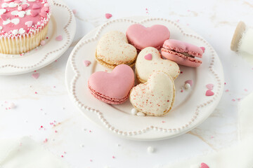 French sweet cookies macarons macaroon with color sprinkles on retro plate on marble table background. Heart shape macarons, cupcake and decor. Mockup greeting card with copy space.