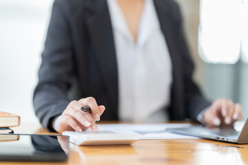 Shot of a young professional woman sitting at desk in front of laptop and using mobile phone working on business contract.