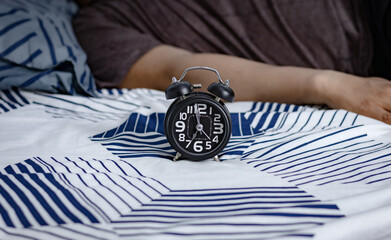 Deadline and Time management concept. Black alarm clock on bed with lazy people still sleeping in...