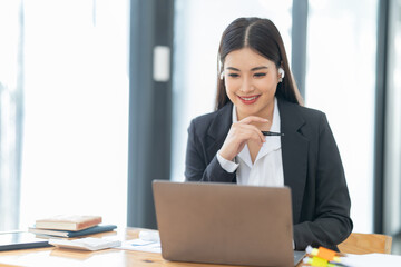 Shot of a young professional woman sitting at desk in front of laptop and using mobile phone working on business contract.