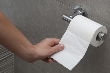 Close up of hand holding toilet paper roll in holder