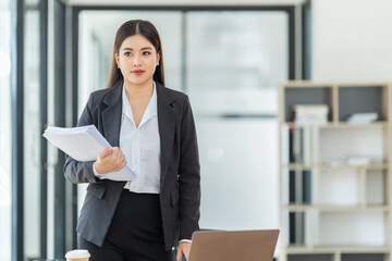 Asian Businesswoman using smartphone for doing finance on an office desk, tax, report, accounting, statistics, and analytical research concept.