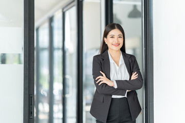 Portrait of beautiful young woman standing in front of glass board and smiling on camera. Female office worker using laptop in company.