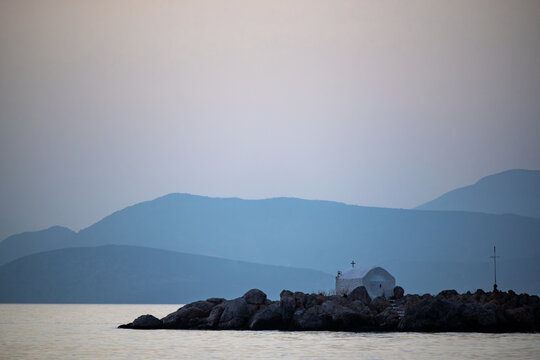 A monastery on a tiny island at sunset viewed from Kamini Harbor on Hydra Island, Greece