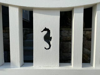 Detail of a white wooden fence with a seahorse shape engraved on a board. Hippocampus carved in...