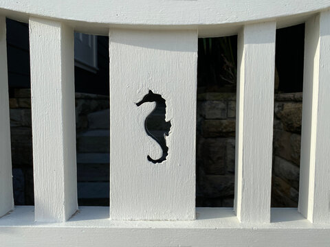 Detail of a white wooden fence with a seahorse shape engraved on a board. Hippocampus carved in wood.