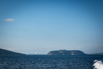 A sailboat glides between two islands on the Saronic Sea between Hydra and the Peloponnese