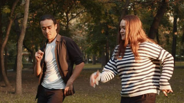 Young asian male dancer and his female partner dancing together cheerfully and fast in a city park on a sunny day. Concept of outdoor active summer leisure