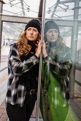 Woman in her mid-thirties with long red hair wearing a cap and black clothing in an urban location.