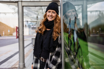 Woman in her mid-thirties with long red hair wearing a cap and black clothing in an urban location.