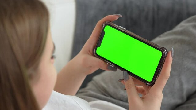 Use green screen for copy space closeup. Chroma key mock-up on smartphone in hand. Woman holds mobile phone iPhone and swipes photos or pictures left indoors of cozy home