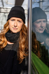 Woman in her mid-thirties with long red hair wearing a cap and black clothing in an urban location.