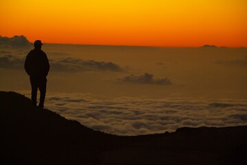 Fototapeta na wymiar Silhouette of a Man Overlooking Sea of Clouds at Sunset