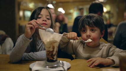 Children Enjoying Ice Cream Sundae Together - Siblings Sharing Dessert at Family Diner During Evening