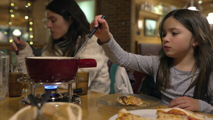 Child eating fondue at restaurant, little girl enjoying traditional Swiss cuisine, putting fork...