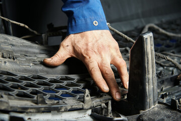 Hands of the master in cars and various car parts. Car engine, bumper, metal parts of the car. The master makes a car repair in a car repair shop.