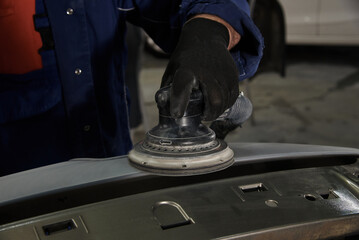 A man at a car maintenance station cleans the car part with an instrument. Preparation of car parts for painting. Car repair at the station. Car service. - 713387980