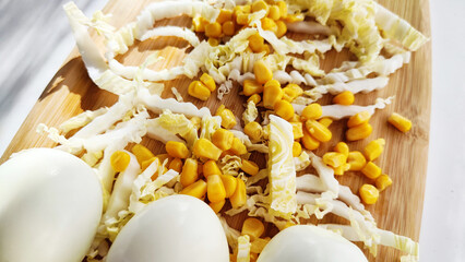 Chopped Peking cabbage, peeled eggs and yellow canned corn on cutting board as a background. Cooking a healthy eco-friendly salad from natural products. Copy space and place for text
