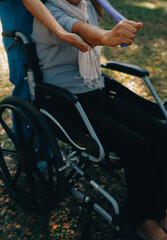 Naklejka premium Young nurse or physiotherapist in scrubs helping a happy retired old woman do fitness exercises with light weight dumbbells at home. Concept of physiotherapy for seniors