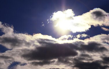Bright light of the sun on a dark blue sky among the clouds.