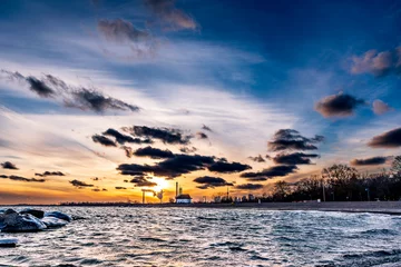 Tuinposter sunset on icy beach in winter with dramatic clouds and  downtown skyline in distant background shot kew beach toronto room for text © Michael Connor Photo