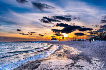sunset on icy beach in winter with dramatic clouds and  downtown skyline in distant background shot...