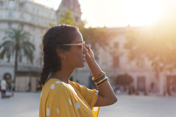 A young hispanic woman wearing a yellow dress with white polka dots, putting on her sunglasses on a...
