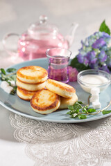 Obraz na płótnie Canvas Fried cottage cheese pancakes syrniki served with sour cream and flower tea on a blue dish.
