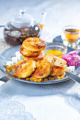Fried cottage cheese pancakes syrniki with raisins and grapes on a blue dish served with black tea.