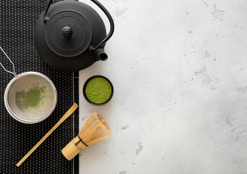 Japanese iron kettle with matcha green tea powder with whisk and spoon and bowl with sifter on white background.Top view.